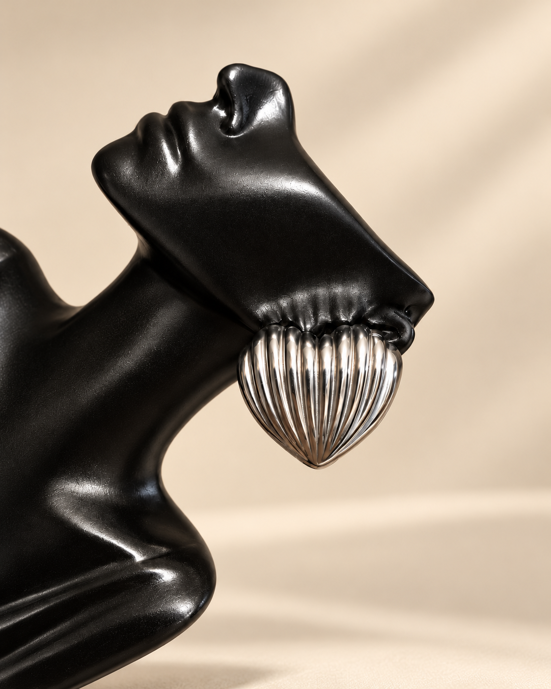 Close-up of ribbed silver heart stud earring showing dimensional vertical grooves