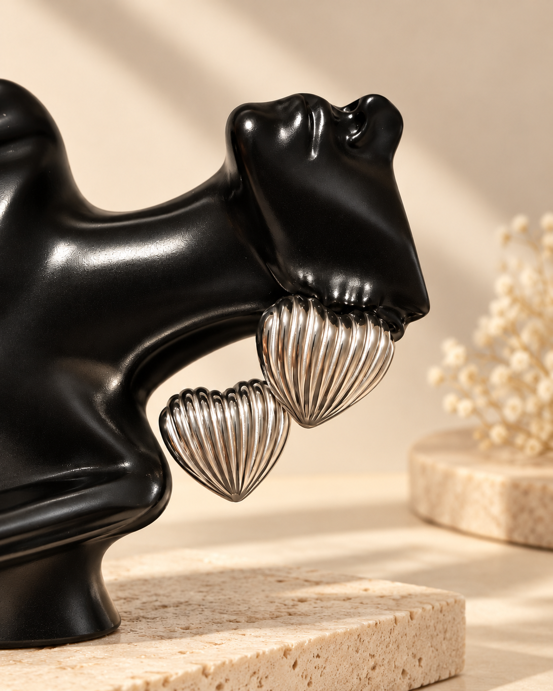 Pair of silver ribbed heart stainless steel stud earrings displayed on black sculpture with cream boutique background